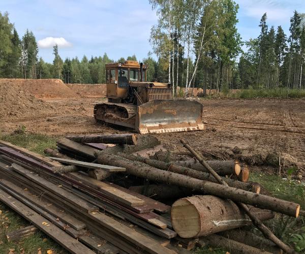 Bulldozer clearing land with cut logs and stacked lumber in the foreground.