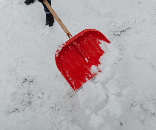 Red snow shovel clearing heavy snow from a driveway during winter conditions.