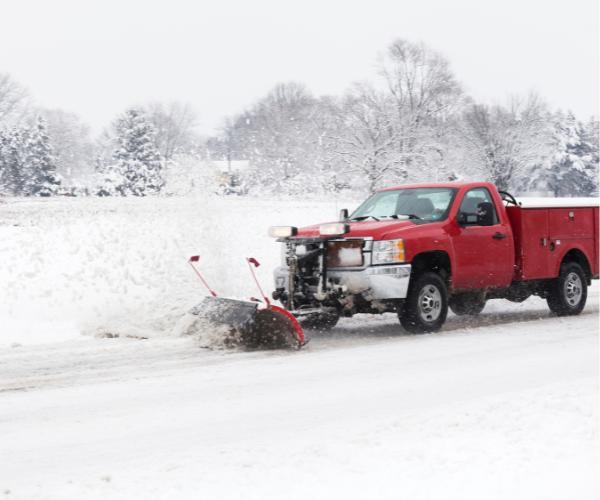 Snow plow truck clearing a snow-covered road, providing professional snow plowing service.