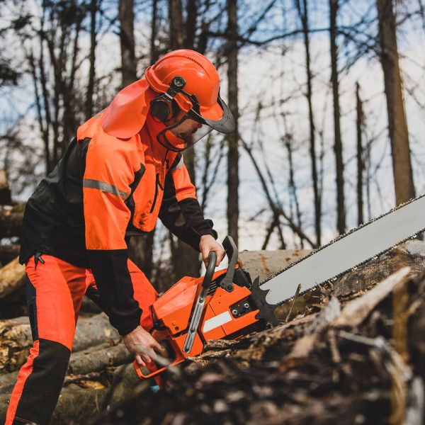Certified Arborist in proper safety gear using a large chainsaw to cut up tree removal debris.